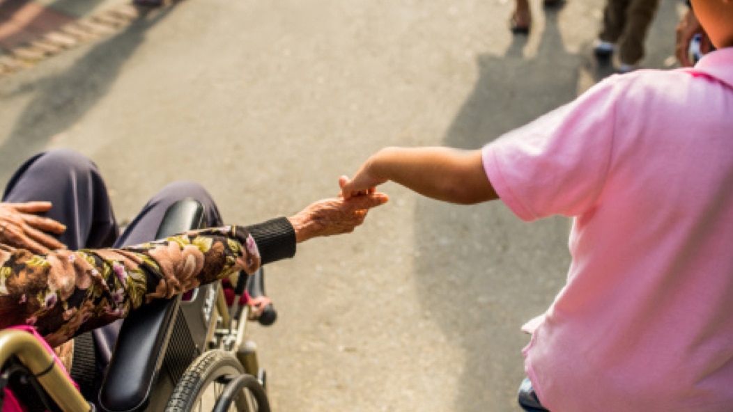 Two people holding hands, with one of the people using a wheelchair.